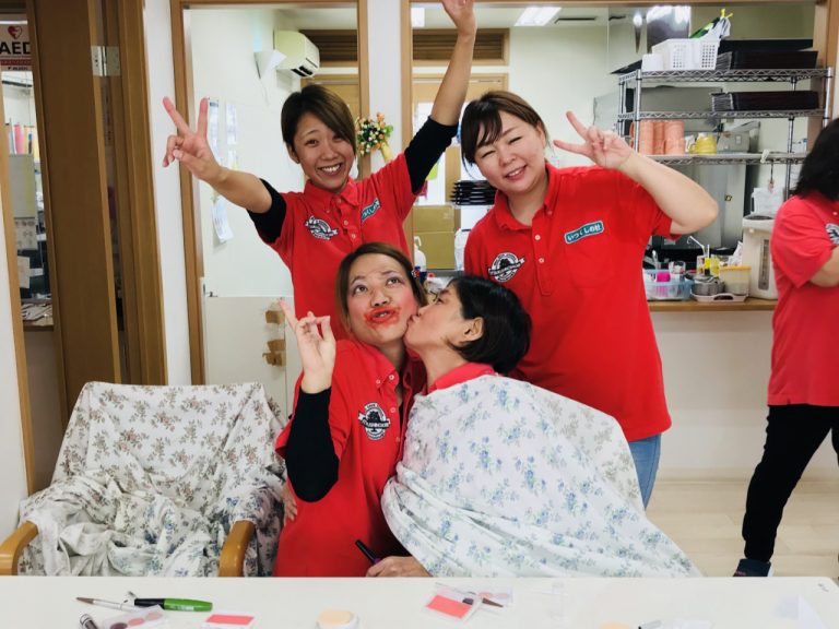 赤いユニフォームのスタッフと入居者が笑顔で触れ合う活動風景